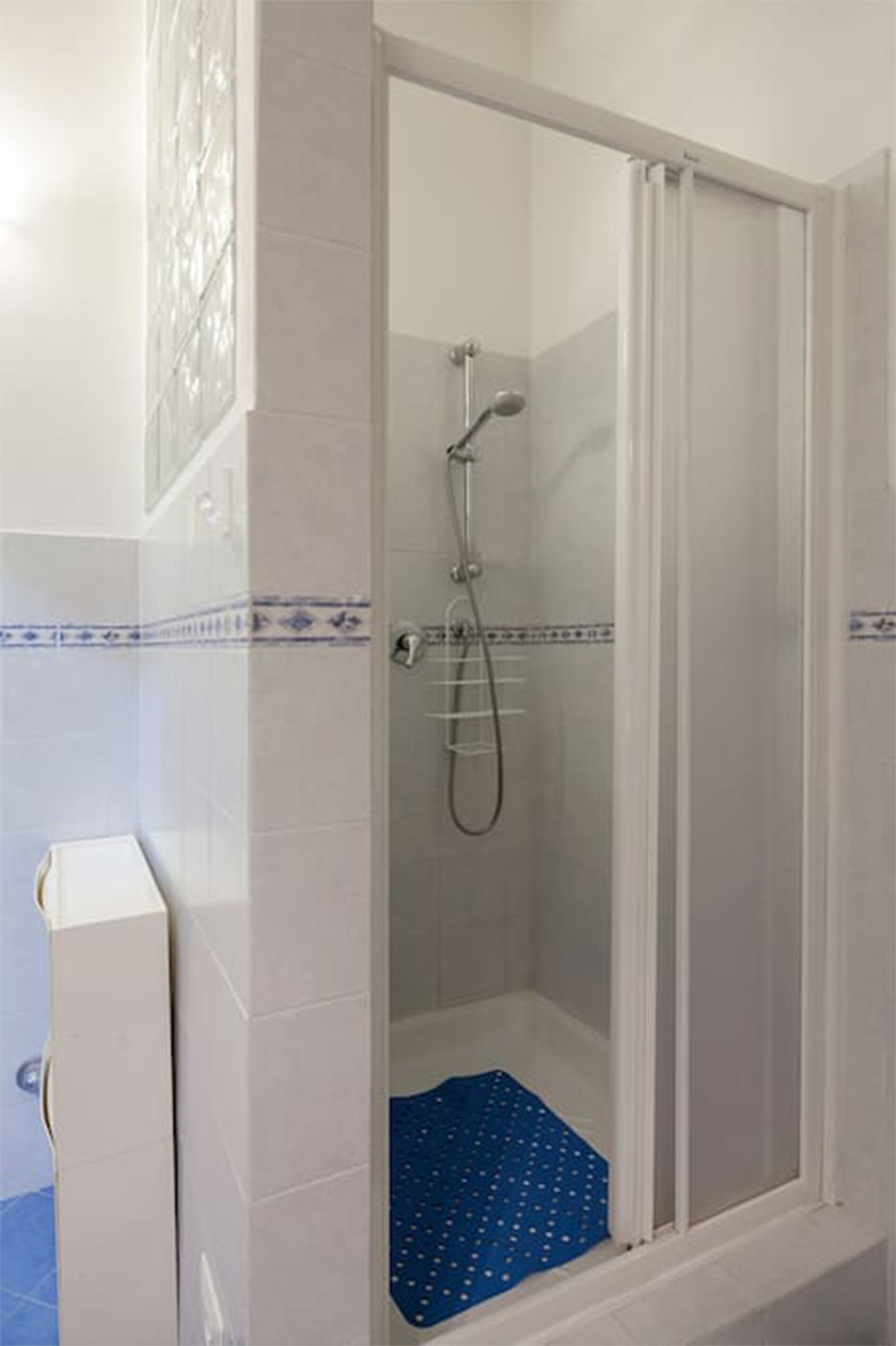 A shower with a glass door, a blue mat, and white tiled walls.
