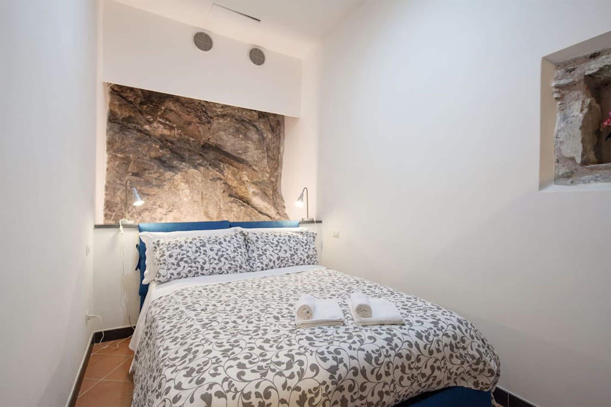 A bedroom with a bed, a large rock-like wall decoration, and a small window with a view of the outside.