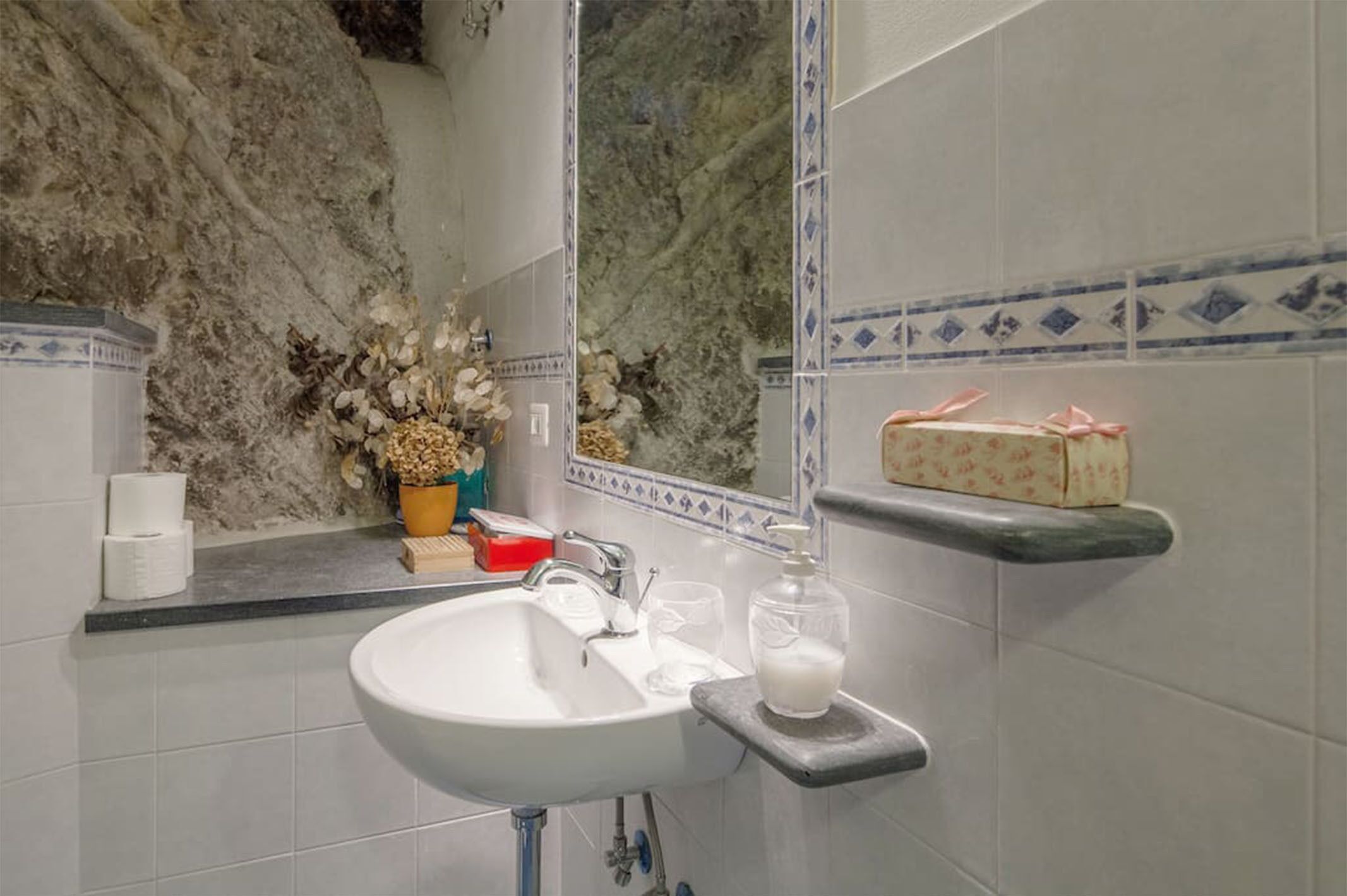 A bathroom with a white sink, a mirror, and a shelf with toiletries.