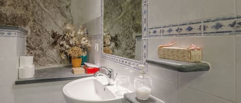 A bathroom with a white sink, a mirror, and a shelf with toiletries.