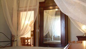 Ein Schlafzimmer mit Holztür, einem Bett mit Metallgestell und transparenten Vorhängen.