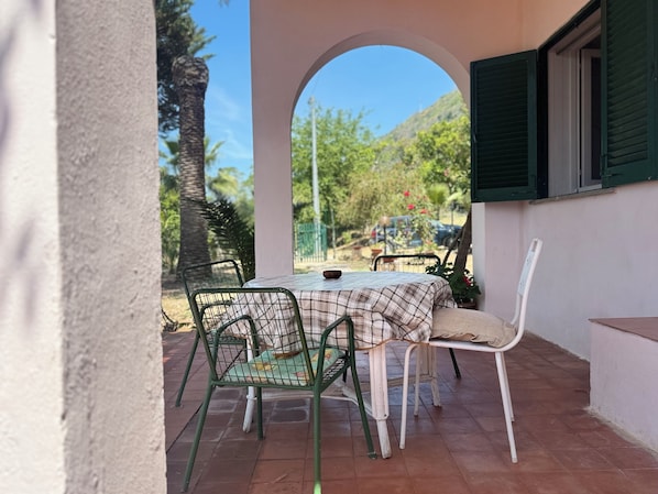 Une terrasse avec une table et des chaises, une arche et une vue sur la verdure et les voitures garées.