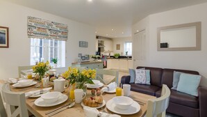 Un coin repas avec une table en bois mise pour le petit-déjeuner, un canapé en cuir marron et une cuisine en arrière-plan.