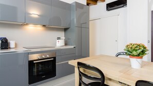 A modern kitchen with grey cabinets, a built-in oven, and a wooden dining table with chairs.