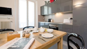 A modern kitchen with grey cabinets, a wooden dining table, and a TV mounted on the wall.