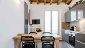 A modern kitchen with a wooden dining table, black chairs, a TV mounted on the wall, and a built-in oven.