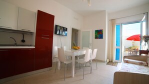 Una cocina moderna con armarios blancos y rojos, una mesa de comedor con sillas y un televisor montado en la pared.