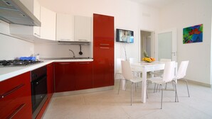 Una cocina moderna con armarios rojo y blanco, una estufa a gas y un comedor con sillas blancas y una mesa.