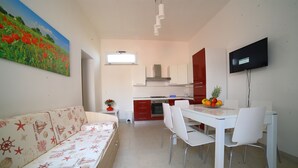 Una cocina moderna con comedor, un sofá de estilo náutico y un televisor montado en la pared.