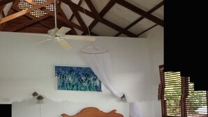 Un dormitorio con una cama de madera, un ventilador de techo, una mesita de noche y un cuadro en la pared, además de una ventana con persianas.