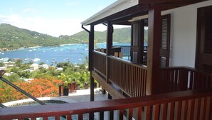 Un balcón de madera con vistas a una bahía con barcos y vegetación.