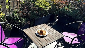 Une terrasse sur le toit, avec une table dressée pour le dîner, entourée d’une végétation luxuriante et offrant une vue panoramique sur les montagnes.