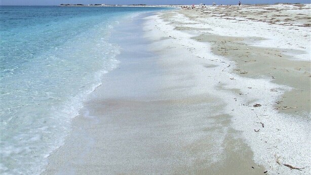 Une plage à l’eau turquoise et limpide et au sable blanc.