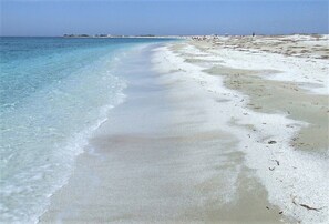 A beach with clear water, sandy shore, and distant buildings.