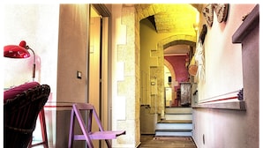 Un couloir étroit avec un plancher en bois, une chaise rouge, une chaise violette et une lampe rouge.