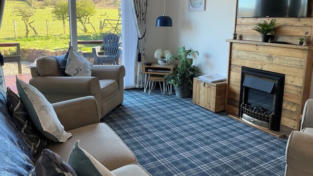 Ein Wohnzimmer mit einer Couch, Sesseln, einem Kamin und Blick auf eine grüne Landschaft.