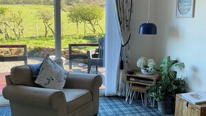 Ein Wohnzimmer mit beigefarbenem Sofa, einem karierten Teppich, einem Esstisch mit Stühlen, einer hängenden blauen Pendelleuchte, einem Blumentopf und einem gerahmten Bild an der Wand.