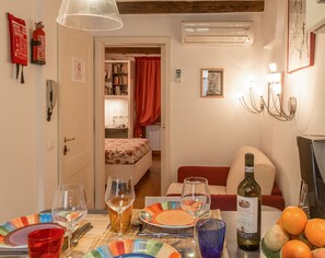 A dining area with a table set for two, a bottle of Chianti wine, and a bowl of oranges.