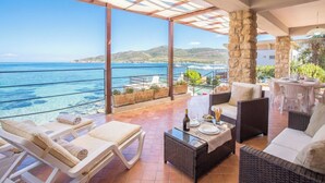 A terrace with wicker furniture, a table with a bottle and glasses, and a view of the sea. - ClickSardegna Villa Flavia with seafront terrace in the Porto Conte Nature Park (Alghero)