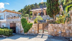 A modern two-story house with a stone facade, a gated entrance, and a balcony overlooking the garden. - ClickSardegna Villa Flavia with seafront terrace in the Porto Conte Nature Park (Alghero)