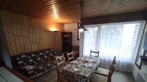 A cozy living room with a wooden ceiling, a sofa with a heart pattern, and a dining table set for four.