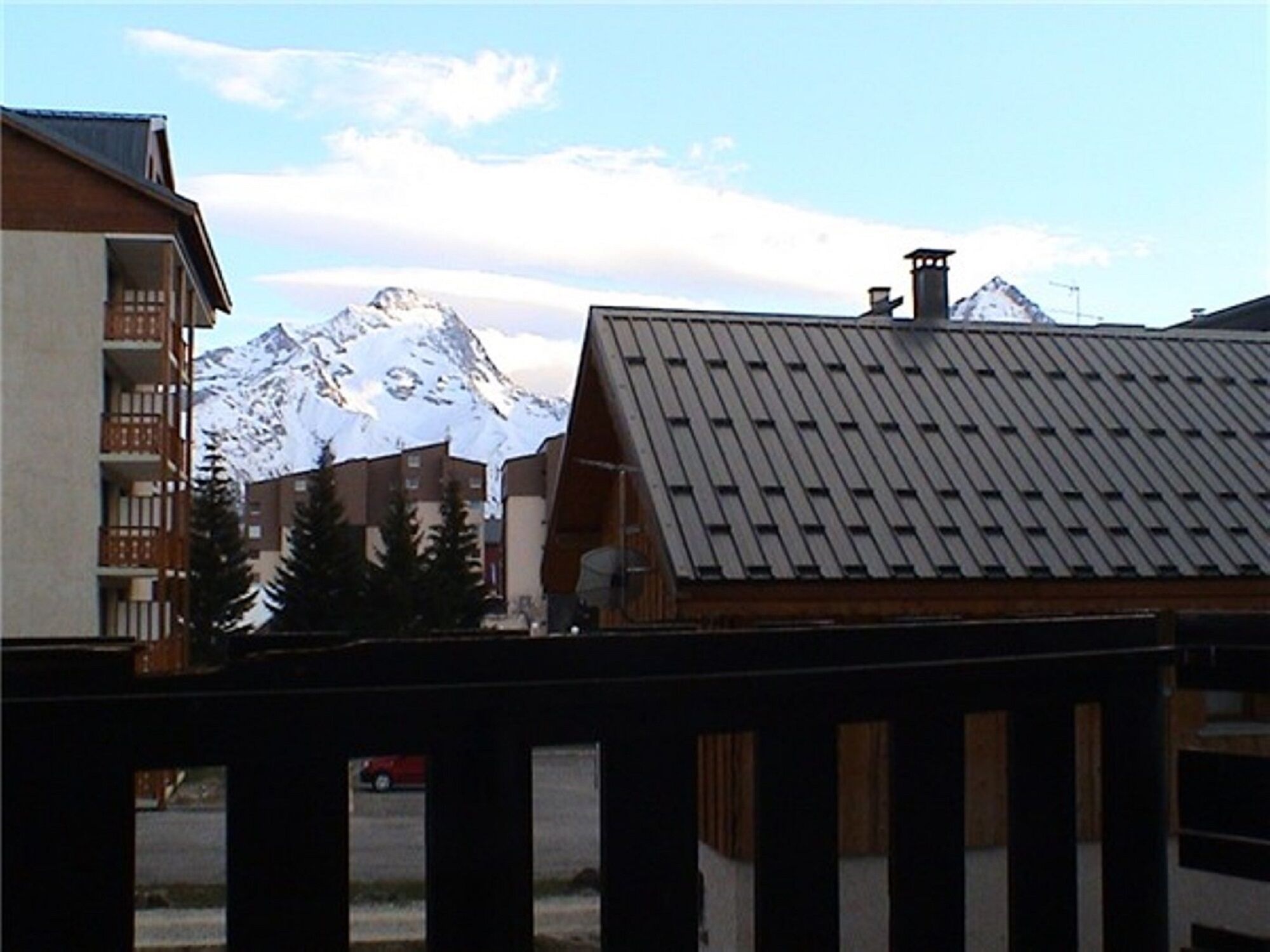 A mountain view with a wooden building and a red car in the foreground.