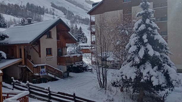 A snow-covered building with a wooden staircase and a snow-covered tree in front.