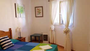 Ein Schlafzimmer mit Bett, Nachttisch, Tisch, einem Fenster mit Vorhängen und Wandbildern.
