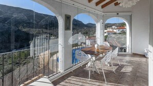 En balkon med et træbord og hvide stole, der kigger ud over et bjergrigt landskab.