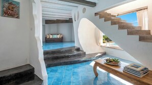A modern interior with a staircase leading to a balcony, a dining area with a table and chairs, and a wall-mounted picture.