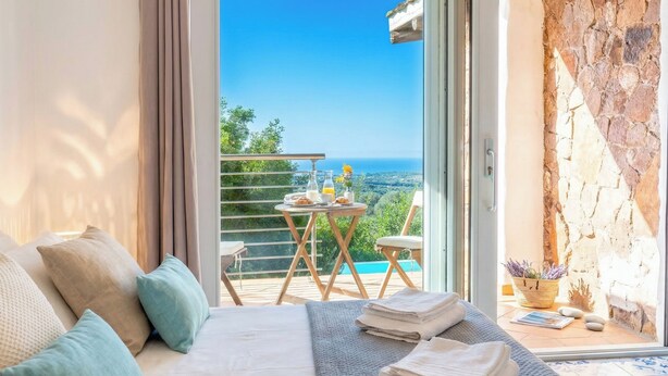 A bedroom with a bed, pillows, a table with breakfast items, and a view of the sea.