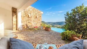 A stone-walled room with a pool, outdoor seating, and a view of the countryside.