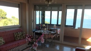 A room with a sofa, a dining table set for two, and a view of the sea through large windows.