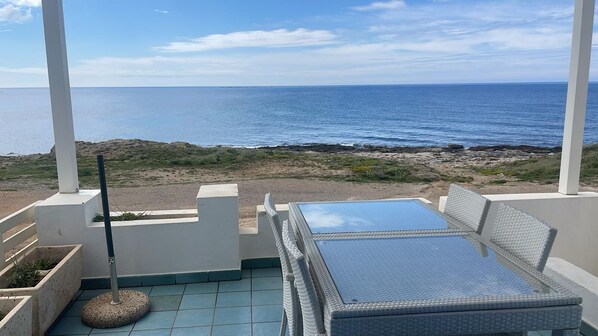 A balcony with a view of the ocean, a table and chairs, and a small garden area.