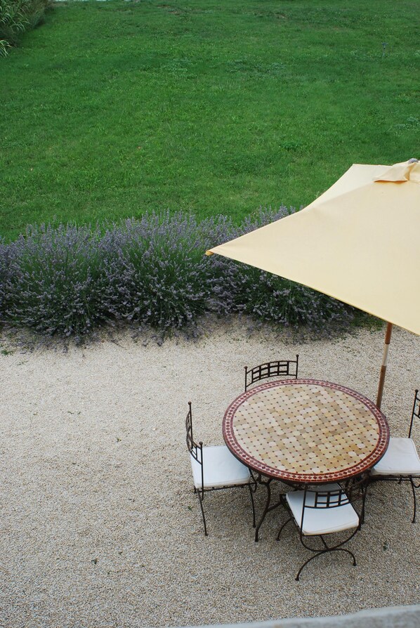 A round table with four chairs and a large umbrella in a gravel area. - Charming house in the heart of the vineyards (Tarascon)