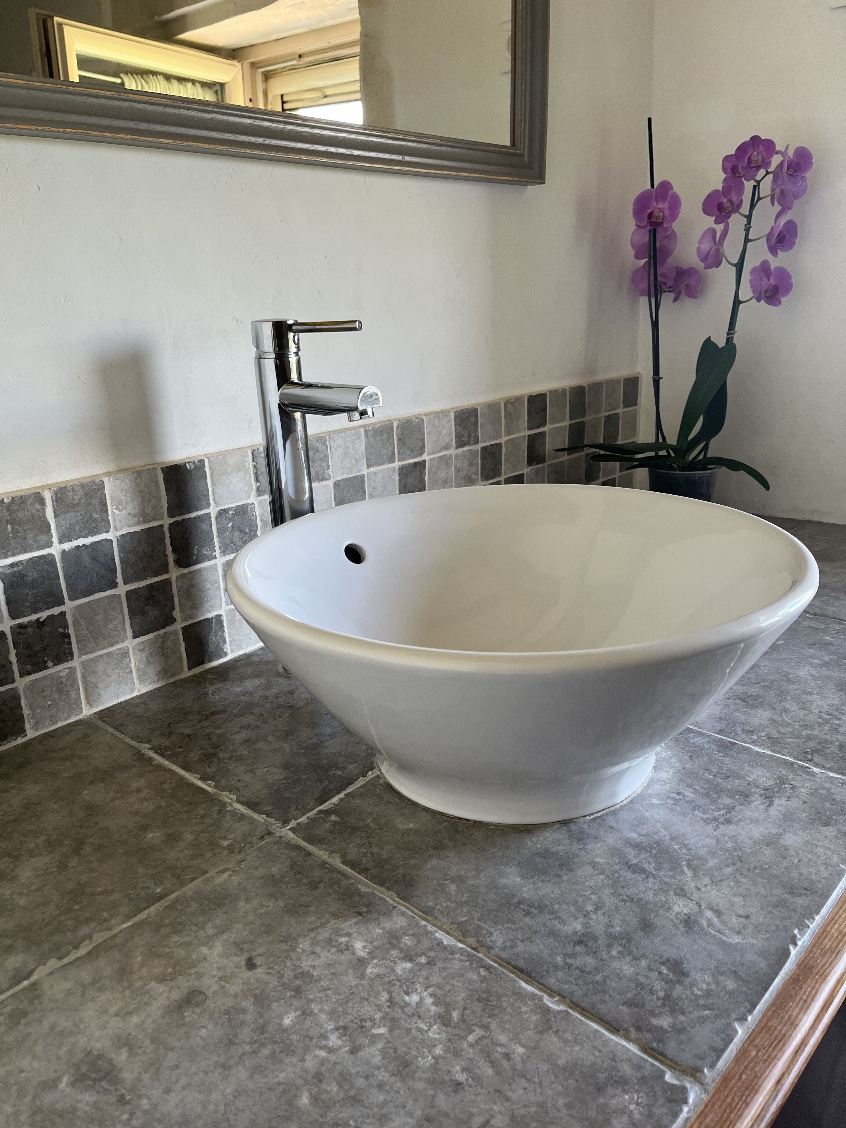 Un bagno con un lavandino in ceramica bianca, un rubinetto cromato e uno schienale piastrellato.