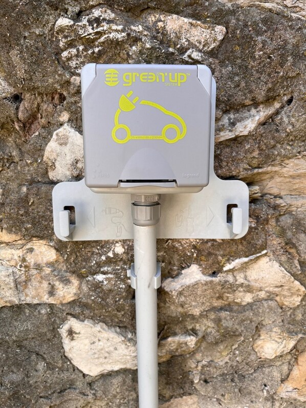 Une borne de recharge pour trottinettes électriques grise, dotée d’un logo et d’une inscription jaunes, fixée sur un poteau blanc, avec un arrière-plan rocheux.