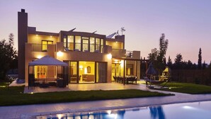 Ein modernes, zweistöckiges Haus mit Swimmingpool, Sitzgelegenheiten im Freien und einer überdachten Terrasse.