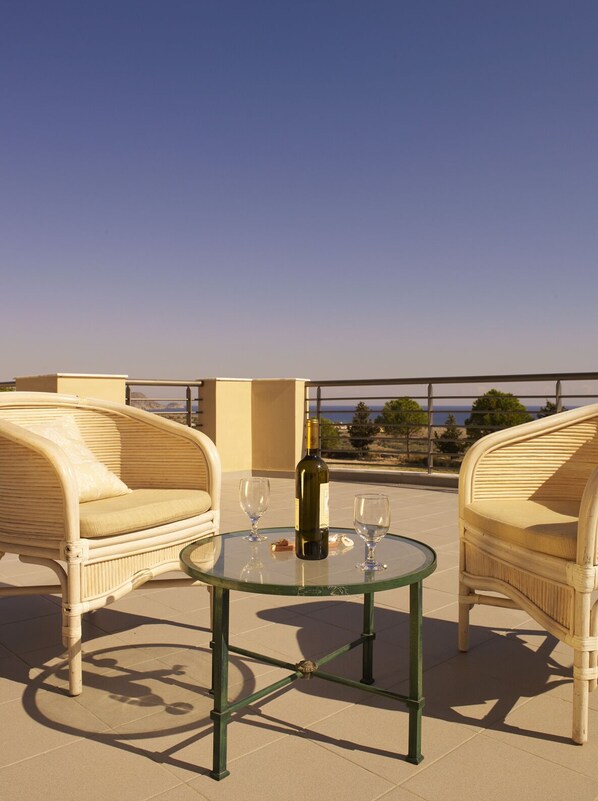 A terrace with wicker chairs and a glass table, a bottle of wine, and two wine glasses.