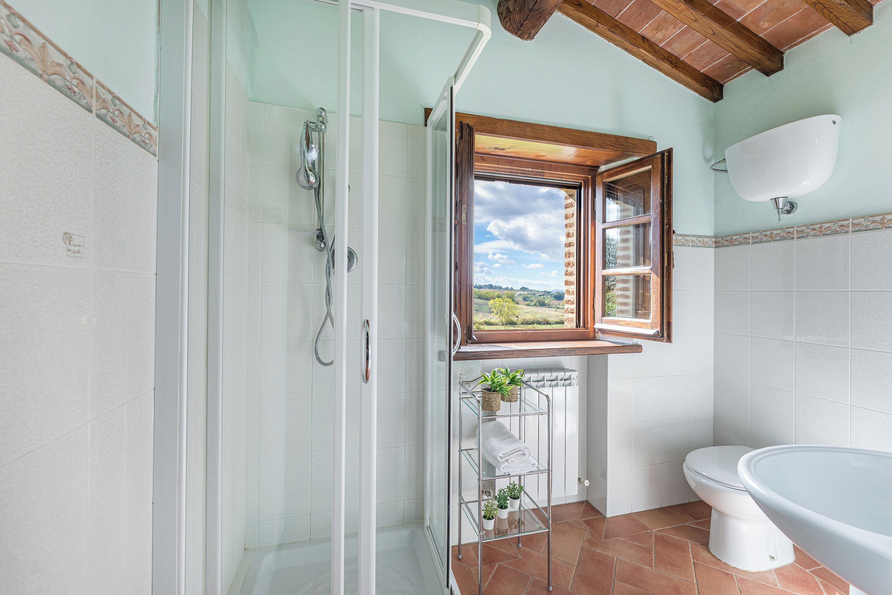 Ein Badezimmer mit Dusche, Toilette und einem Fenster mit Blick ins Freie.