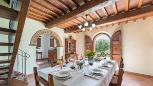 A dining area with a long table set for a meal, wooden beams on the ceiling, and arched doorways.