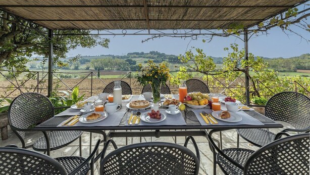 An outdoor dining area with a table set for breakfast, surrounded by chairs, and overlooking a scenic landscape.