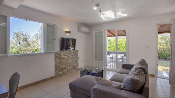 Una sala de estar moderna con una pared de acento de piedra, un televisor de pantalla plana, una mesa de centro de vidrio y un sofá gris.