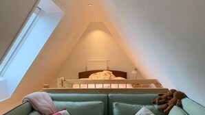 A cozy loft bedroom with a sloped ceiling, a bed with a wooden headboard, and a green sofa with floral cushions. - The Best of Both Worlds - Peaceful Countryside Living with Easy Access to Munich (Reichertshausen)