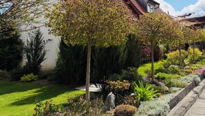 A house with a red-tiled roof, surrounded by a well-maintained garden with various plants and a lawn. - The Best of Both Worlds - Peaceful Countryside Living with Easy Access to Munich (Reichertshausen)