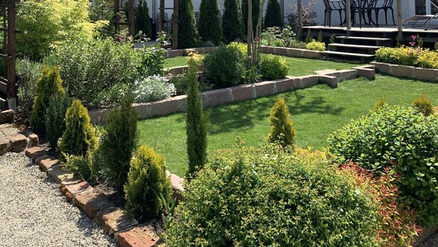A two-story house with a red-tiled roof, a garden with various shrubs and a small tree, and a wooden pergola. - The Best of Both Worlds - Peaceful Countryside Living with Easy Access to Munich (Reichertshausen)