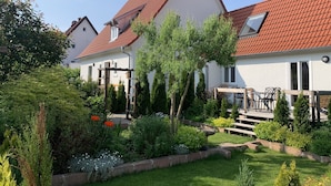 A two-story house with a red-tiled roof, a garden with various plants and a wooden deck. - The Best of Both Worlds - Peaceful Countryside Living with Easy Access to Munich (Reichertshausen)