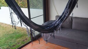 A hammock hanging between two windows on a tiled patio, with a sofa and a table nearby.