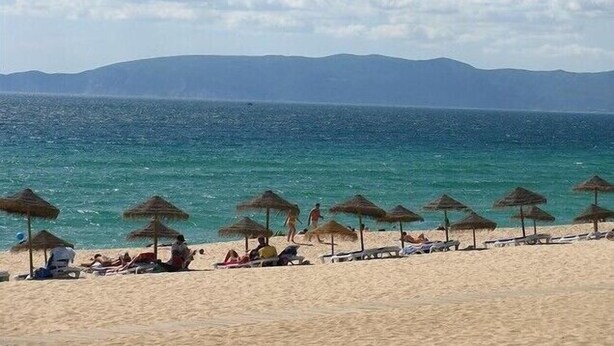A beach with thatched umbrellas and sun loungers.