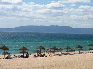 Een strand met rieten parasols en ligbedden.